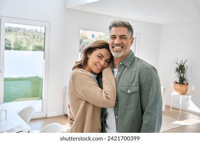 Smiling middle aged mature couple embracing standing at home. Happy romantic affectionate senior older man and woman in love enjoying hugging looking at camera in modern house living room. Portrait. - Powered by Shutterstock