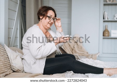Smiling middle aged plus size woman using mobile phone on bed at home