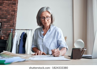 Smiling Middle Aged Stylish Woman Fashion Designer Drawing Sketches In Studio. Mature Old Adult Elegant Grey-haired Lady Dressmaker Small Business Owner Creating New Fashion Design Cloth In Atelier.