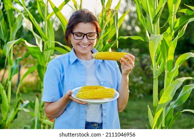 Smiling Middle Aged Woman Eating Boiled Ripe Corn On The Cob