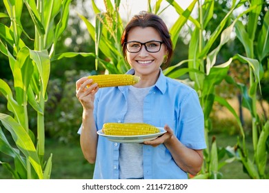 Smiling Middle Aged Woman Eating Boiled Ripe Corn On The Cob