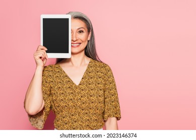 Smiling Middle Aged Woman Obscuring Face With Digital Tablet Isolated On Pink