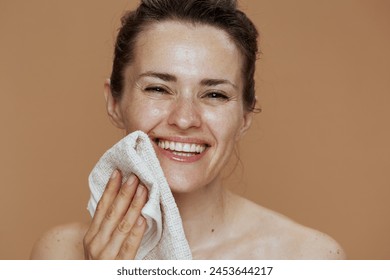 smiling middle aged woman with towel washing face against beige background. - Powered by Shutterstock