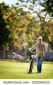 Smiling middle aged woman walking with her bicycle in the park.