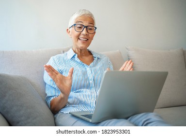 Smiling Middle Aged Woman Waving Hand Looking At Camera, Older Mature Lady In Glasses Making Video Blog Or Call At Home, Happy Friendly Senior Vlogger Sitting On Sofa Dating Online, Headshot Portrait