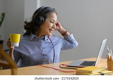 Smiling Middle Aged Woman Wearing Headphone Watching Online Webinar, Working At Home With A Laptop Computer