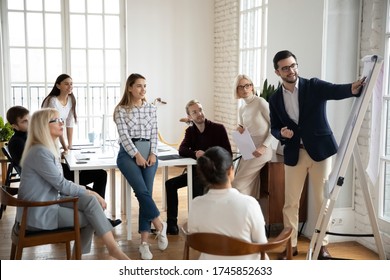 Smiling Middle Aged And Young Focused Managers Listening To Motivated Male Speaker Lecturer At Workshop. Happy Businessman Coach Trainer Showing Marketing Research Results On Flipchart To Colleagues.