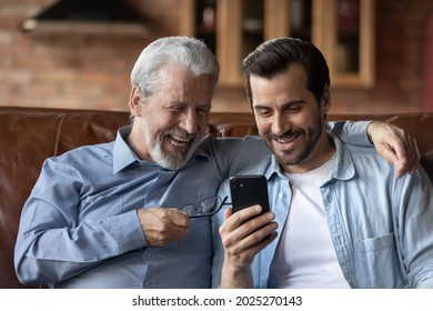 Smiling middle-aged 60s father and grownup man child relax together talk speak on video webcam call on smartphone. Happy old dad and adult son rest at home look at cellphone screen browse web. - Powered by Shutterstock