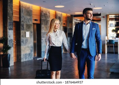 Smiling Middle-aged Couple Holding Hands And Walking In The Lobby Of The Fancy Hotel. They Going Into Their Room. The Woman Is Pulling A Suitcase.