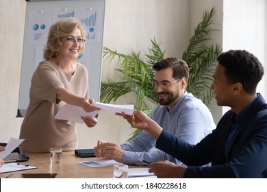 Smiling middle-aged female trainer or coach lead meeting or training in office share handout materials to employees. Happy businesswoman give document paperwork to diverse workers at briefing. - Shutterstock ID 1840228618