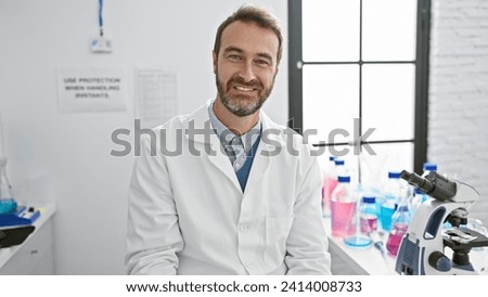 Smiling middle-aged hispanic man in lab coat indoors with microscope and lab equipment, portraying a professional and welcoming healthcare worker.
