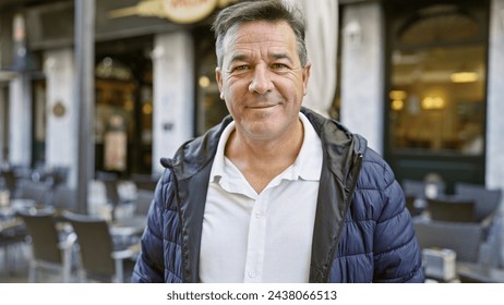 Smiling middle-aged man in casual attire enjoys outdoor seating at an urban cafe, embodying leisure in the city. - Powered by Shutterstock