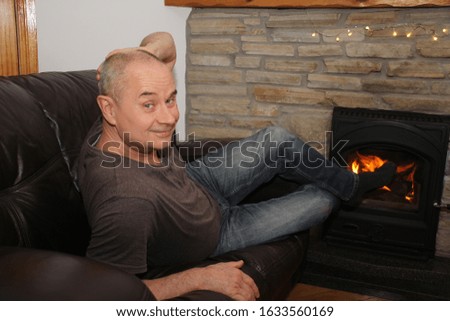 smiling middle-aged man lies on a sofa near a burning fireplace, winter relaxation concept