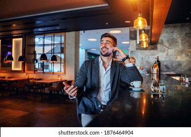 Smiling Middle-aged Man Sitting In A Bar Of A Fancy Hotel And Talking On The Phone.