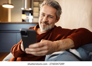Smiling middle-aged man using smartphone at home