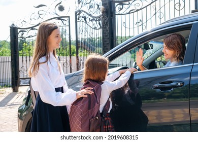 Smiling Middle-aged Mother In The Car, Leaving Her Daughters And Sisters In School Uniform At School And Gesturing Goodbye.