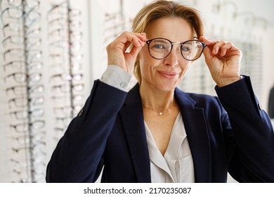 Smiling Middle-aged woman chooses glasses in an optics store - Powered by Shutterstock