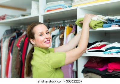 Smiling Middle-aged Woman Choosing Apparel On Shelves At Store