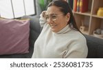 Smiling middle-aged woman with glasses, sitting comfortably in a cozy home interior.