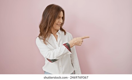 A smiling middle-aged woman with short hair, wearing a white shirt, points to something off-camera against a pink background. - Powered by Shutterstock