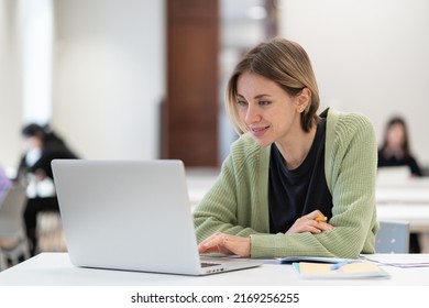 Smiling Middle-aged Woman Studying Online On Laptop Computer While Sitting In Classroom, Doing Second Degree As Mature Student. Happy 45s Female Attending Online Professional Development Course