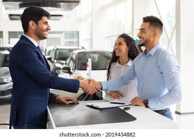 Smiling middle-eastern young man and woman buying car at auto salon, handsome arab guy shaking sales assistant hand, making successful deal, happy family got brand new luxury car, side view - Shutterstock ID 2019434882