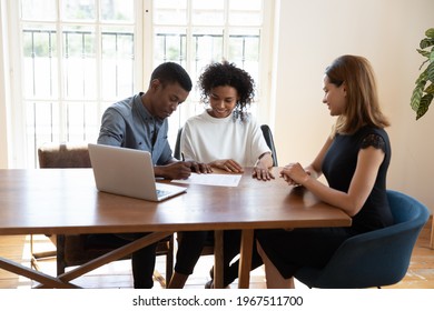 Smiling Millennial African American Family Couple Signing Contract Agreement With Female Real Estate Agent At Office Meeting, Discussing Deal Terms Of Conditions, Purchasing Renting Leasing Apartment.