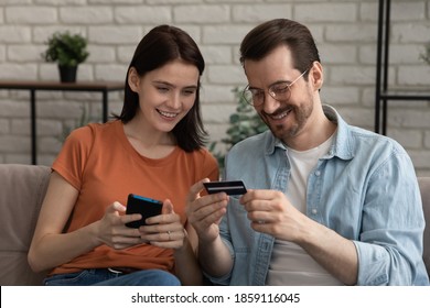 Smiling Millennial Caucasian Couple Involved In Online Shopping, Entering Payment Information From Credit Bank Card In Mobile Application, Satisfied With Quick Money Transfer, Modern Tech Concept.