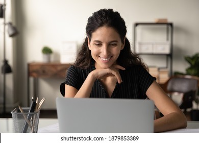 Smiling Millennial Caucasian Female Look At Laptop Screen Browse Surf Wireless Internet. Happy Young Woman Work Online On Computer Gadget At Home Office, Watch Video Or Webinar. Technology Concept.