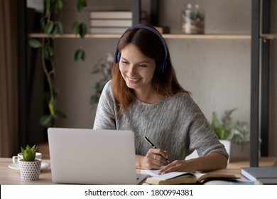 Smiling millennial Caucasian girl in headphones sit at desk look at laptop screen study online, happy smart young woman in earphones take web course or training on computer, distant education concept - Shutterstock ID 1800994381