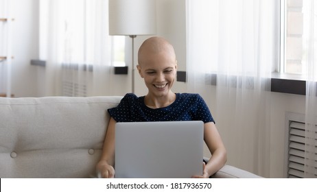 Smiling Millennial Caucasian Hairless Sick Woman Suffer From Oncology Relax Sit On Sofa At Home, Watch Funny Video On Laptop. Happy Young Ill Bald Female With Cancer Browse Internet Use Computer.