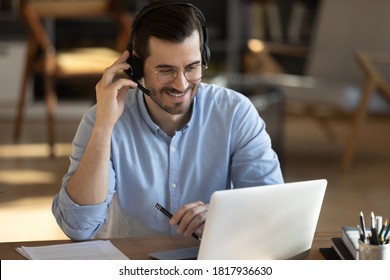 Smiling millennial Caucasian man in headset look at laptop screen work online from home office. Happy young man in headphones watch webinar take course or training on web. Distant education concept.