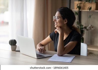 Smiling Millennial Caucasian Woman In Glasses Sit At Desk At Home Office Work Online On Computer. Happy Young Female In Spectacles Use Laptop Study Or Take Distant Course, Look In Distance Dreaming.