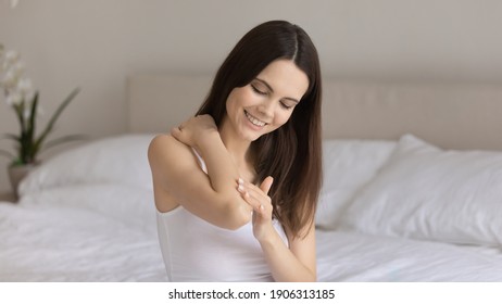 Smiling Millennial Caucasian Woman In Home Bedroom Do Daily Beauty Body Procedures Or Treatment. Happy Young Female Apply Nourishing Moisturizing Body Cream Or Balm For Soft Skin. Skincare Concept.