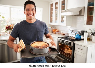 Smiling millennial Hispanic man standing in kitchen presenting the cake he has baked to camera