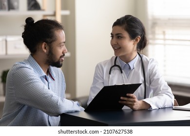 Smiling millennial Indian doctor physician showing good health test result on clipboard to happy young African American male patient, discussing successful illness treatment or medical insurance. - Powered by Shutterstock