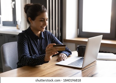 Smiling millennial Indian woman sit at home look at laptop screen shopping online on laptop with credit card. Happy young ethnic female make payment purchase on internet use secure bank system. - Shutterstock ID 1840196818