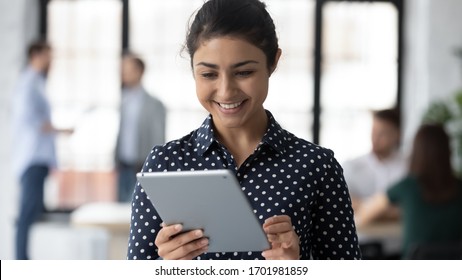 Smiling millennial Indian woman worker browsing wireless Internet on modern tablet in office, happy young biracial female employee texting or messaging, surfing on pad gadget, technology concept - Shutterstock ID 1701981859