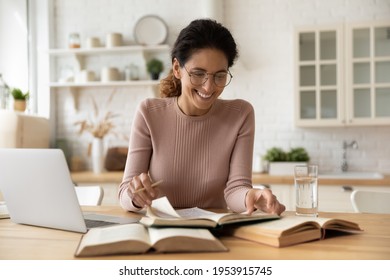 Smiling Millennial Lady Sit At Desk Turn Pages Of Book Read Funny Fact Information In Scientific Literature. Latin Woman Student Prepare For Test Exam Glad To Find Answer On Question At Paper Workbook