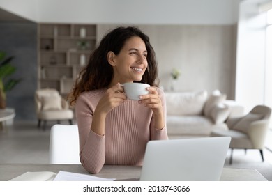 Smiling millennial Latino woman sit at desk at home office work online on computer drink coffee tea from mug. Happy young Hispanic female enjoy morning in cozy living room use laptop for distant job. - Powered by Shutterstock