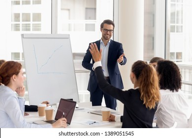 Smiling millennial male coach or presenter make flip chart presentation ask question during work training, motivated confident female employee raise hand answer engaged in teamwork at seminar - Powered by Shutterstock