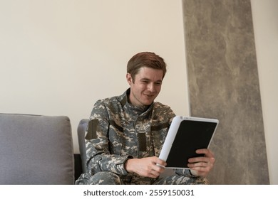 Smiling millennial man in camouflage uniform holding modern digital tablet, chatting with family, posing on white studio background, copy space. Modern technologies and military personnel concept. - Powered by Shutterstock