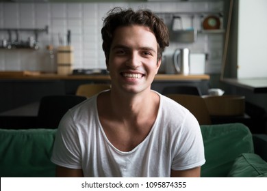 Smiling millennial man head shot portrait, happy handsome young blogger looking at camera sitting on kitchen sofa making video call or shooting blog, cheerful casual friendly guy posing at home - Powered by Shutterstock