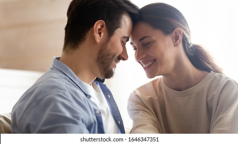 Smiling millennial man and woman touch foreheads hug spend romantic intimate tender weekend at home, happy young couple cuddle relaxing spending time together, relationships romance concept