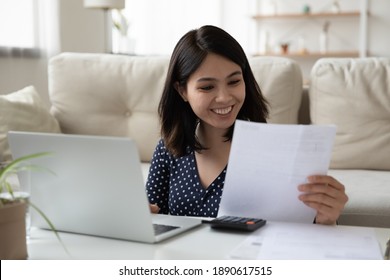 Smiling Millennial Mixed Race Asian Woman Holding Paper Taxes Bills, Managing Monthly Budget Using Calculator And Computer Application, Feeling Happy Of Having Enough Money, Financial Wellbeing.