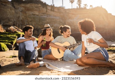Smiling millennial multiethnic people students with bottles, playing guitar, enjoy summer vacation, picnic, have fun on beach. Music lifestyle, spare time, weekend party together - Powered by Shutterstock
