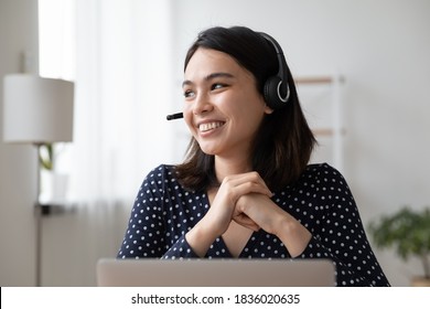 Smiling Millennial Vietnamese Girl In Earphones Distracted From Computer Work Look In Distance Thinking Dreaming. Happy Young Asian Woman In Headphones Make Plans, Visualize Or Imagine Success.