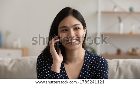 Smiling millennial Vietnamese have pleasant cellphone conversation using wireless internet connection on gadget. Happy young Asian woman have fun speak talk on smartphone call at home