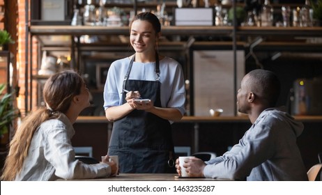 Smiling millennial waitress with notebook taking order from young multiracial client couple, diverse friends relax hang out in cafe or restaurant speak with staff enjoying good service and atmosphere - Shutterstock ID 1463235287