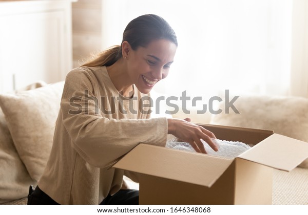 Smiling millennial woman sit on couch at home\
open post package shopping online buying goods on internet, happy\
young female customer unpack postal shipping parcel satisfied with\
order or delivery
